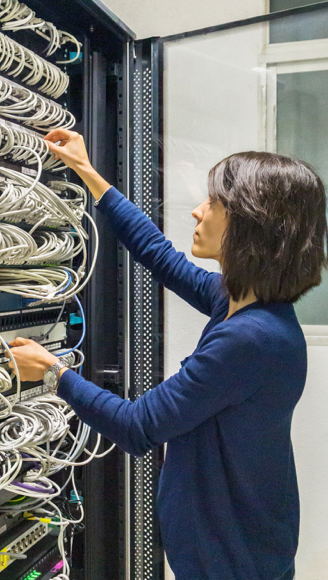 The girl switches fiber-optic Internet wires in a rack with powerful telecommunications.